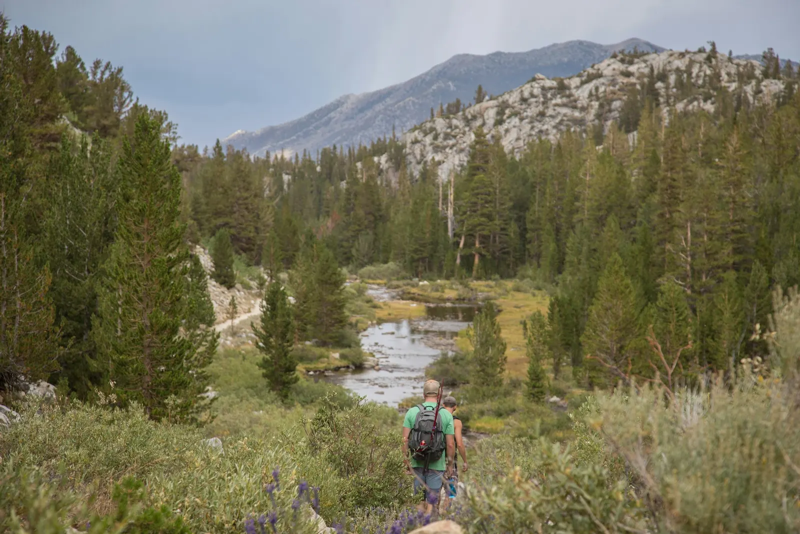 A hiker walking through a green mountain valley below granite peaks