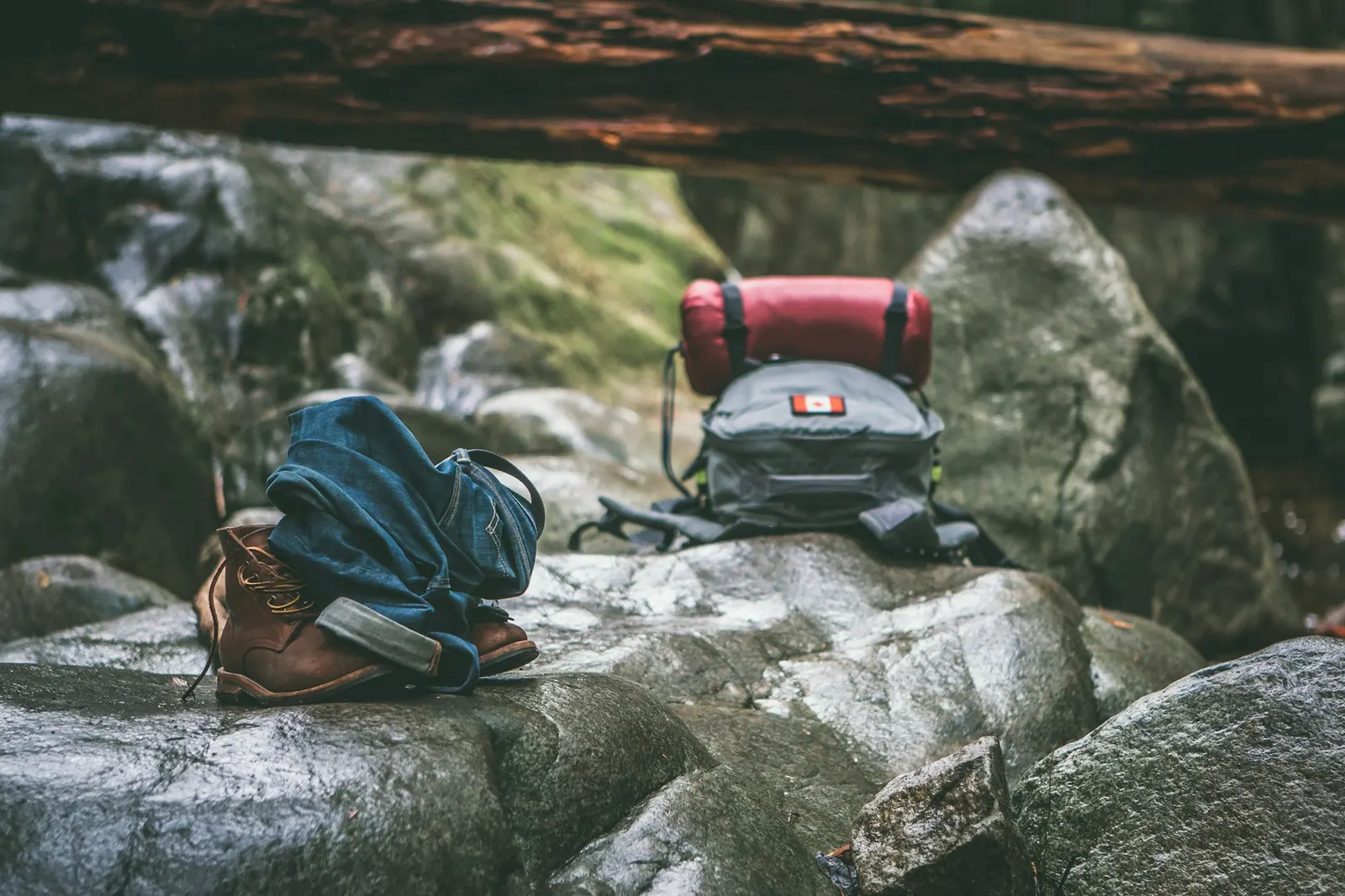 A hiking backpack, boots and camping gear resting on a granite boulder in a forest