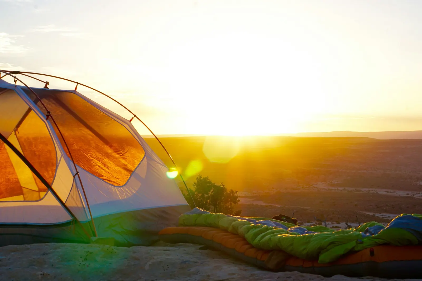 An orange tent with a sleeping bag laid out in golden evening light on a mountain slope