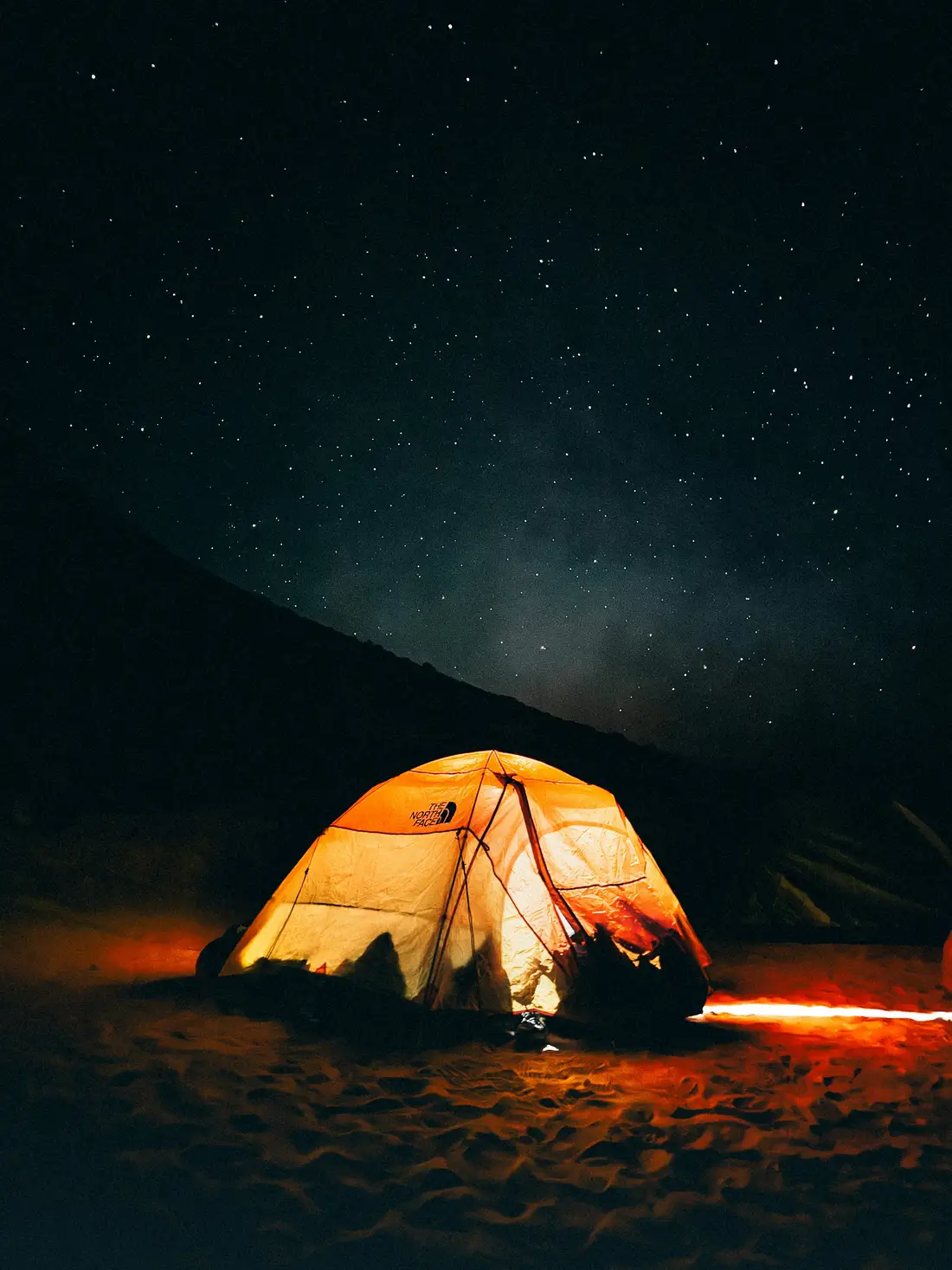 A glowing orange tent beneath a dark sky full of stars on a mountainside