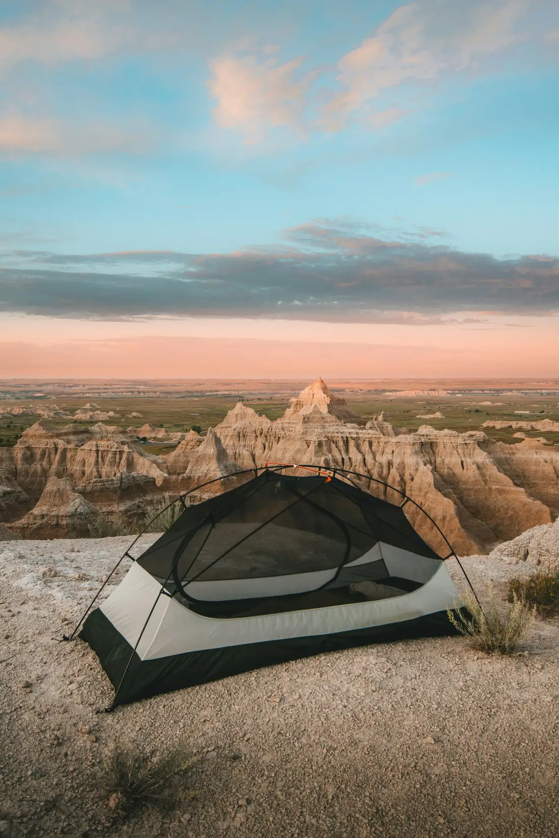 Two tents pitched on a rocky desert overlook above eroded badlands at sunset